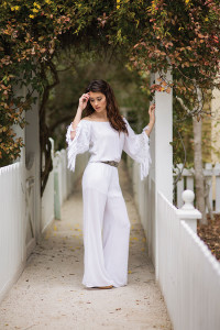 MOODY BLUES BOUTIQUE Julianne looks breathtaking in this off-the-shoulder jumpsuit with fringe detailing on the sleeves. Pair a Pink Pewter belt and cute cork wedges for a chic finish. 