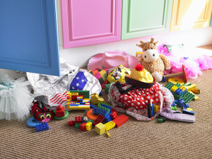 Children's toys and items of clothing strewn on floor near open cupboard door in bedroom